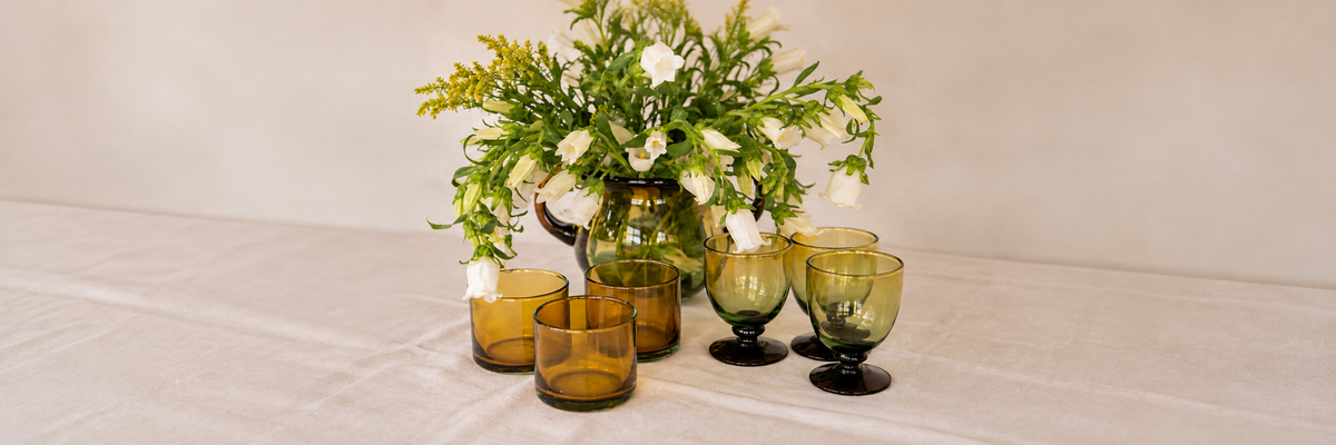 Cristalería artesanal de Pistilo & Gracia con vasos y copas de vidrio soplado en tonos ámbar y verde.