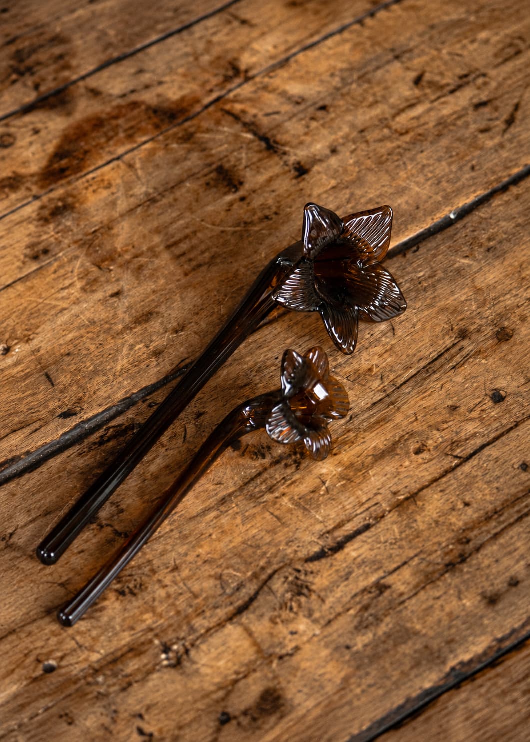 Set de dos apagavelas de vidrio soplado ámbar con forma de flor, sobre superficie de madera rústica.