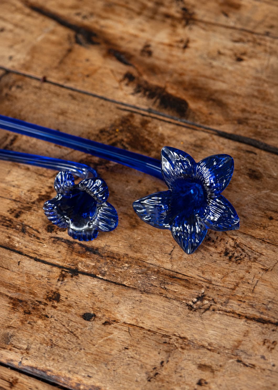 Set de dos apagavelas de vidrio soplado azul con forma de flor, sobre superficie de madera rústica.