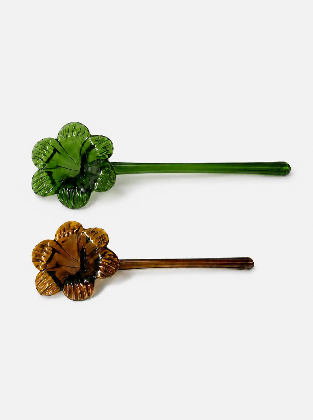 Dos apagavelas de vidrio soplado en colores verde y ámbar, con forma floral y mango alargado.