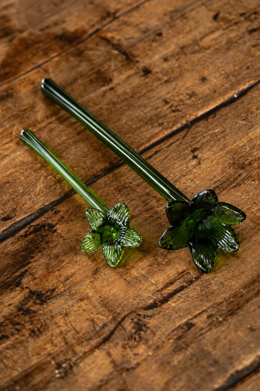 Set de dos apagavelas de vidrio soplado verde con forma de flor, sobre superficie de madera rústica.