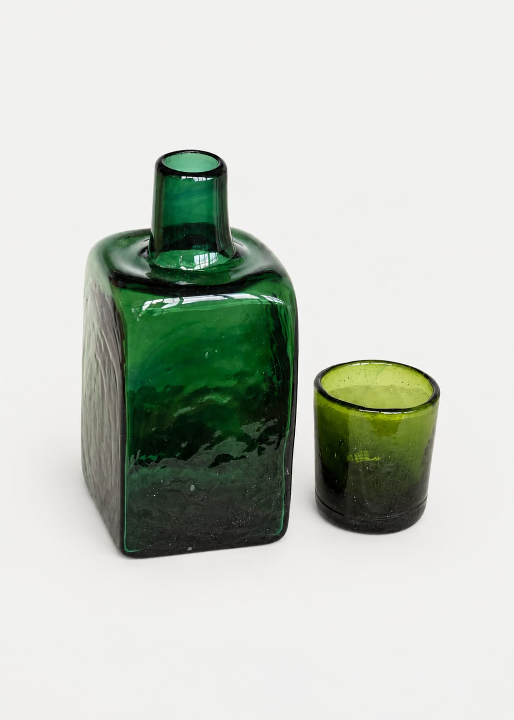 Botella para nochero con vaso en vidrio soplado verde, con vaso separado junto a la pieza.