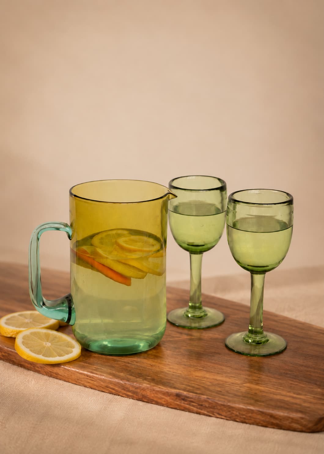 Copas de vino altas verdes de vidrio soplado junto a jarra de vidrio sobre mesa de madera.