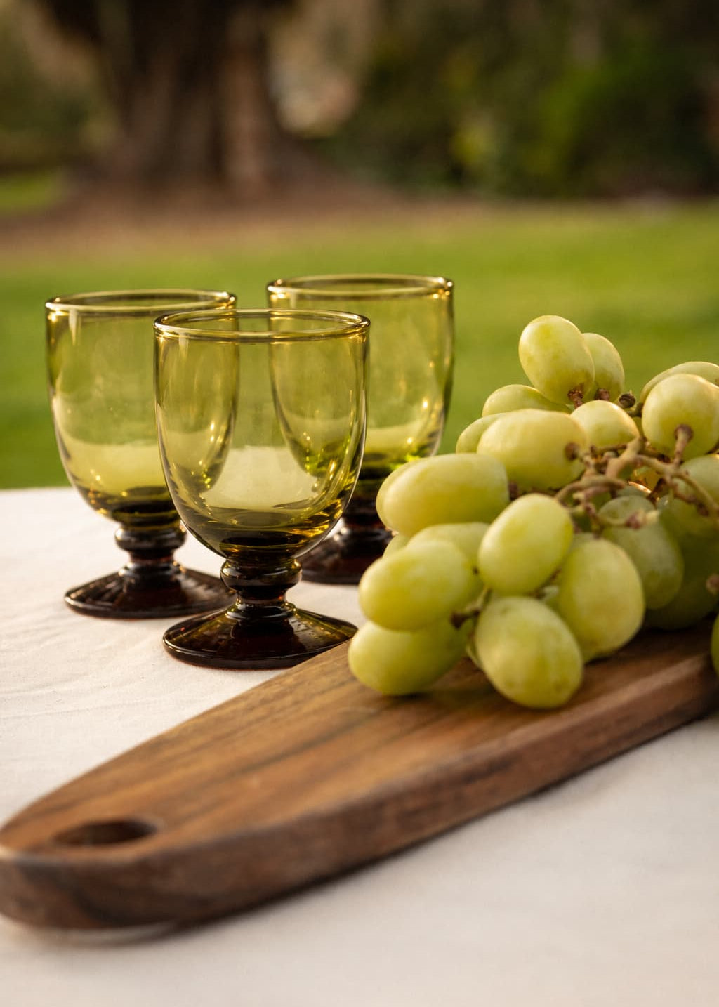 Copas Vino Botón en vidrio soplado ámbar sobre tabla de madera junto a uvas verdes.