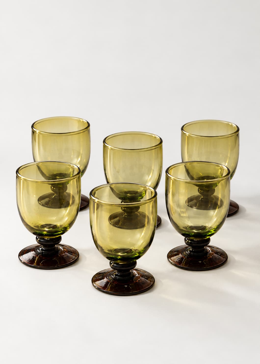 Set de seis Copas Vino Botón en vidrio soplado ámbar sobre fondo neutro.