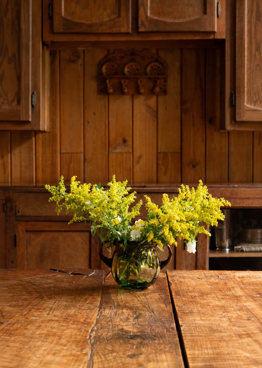 Florero Orejas Ámbar en vidrio soplado con flores amarillas sobre mesa de madera en ambiente de cocina.