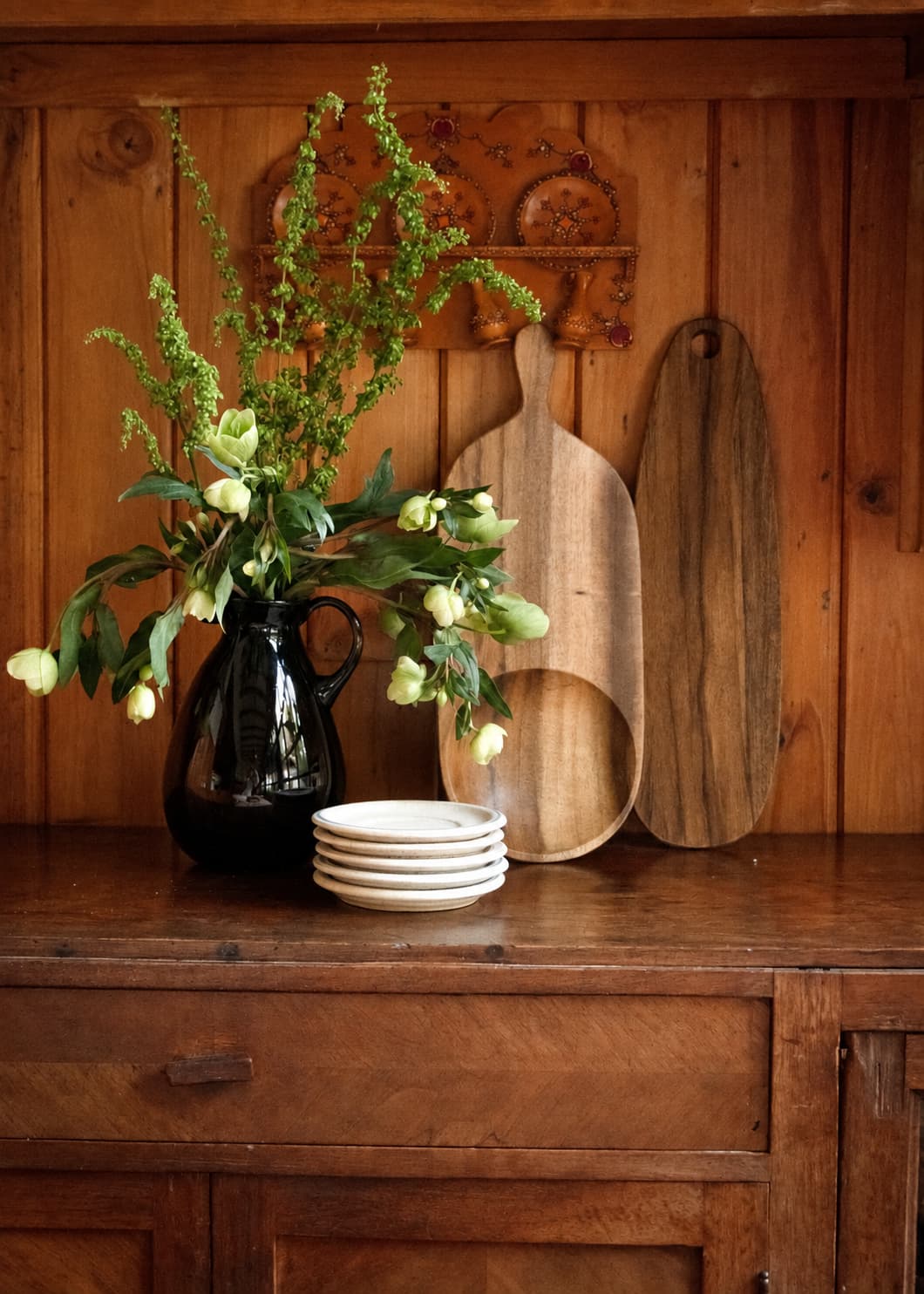 Tablas de madera pequeña y mediana en ambiente de cocina junto a flores y vajilla.