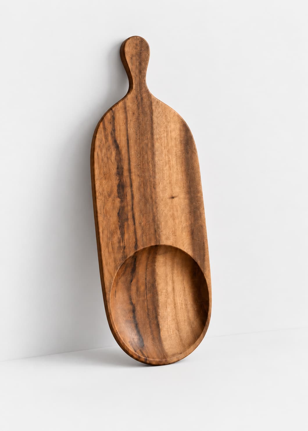 Tabla de madera pequeña artesanal con mango y cavidad circular, vista frontal.