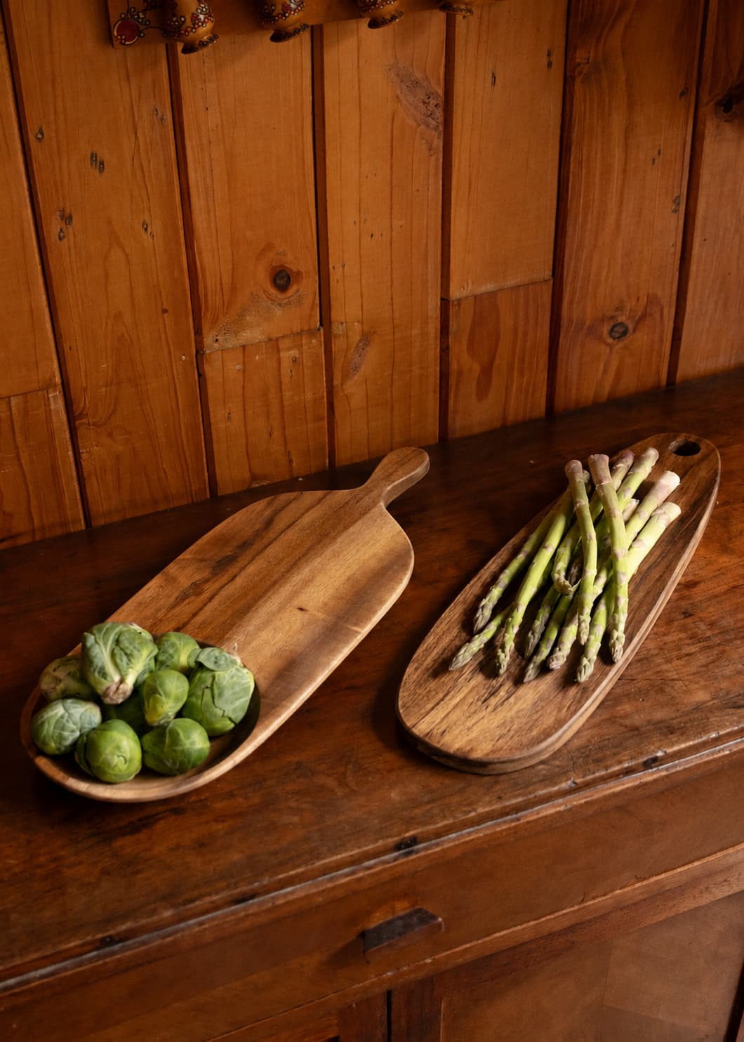 Tabla de madera pequeña con espárragos y tabla de madera mediana con coles de Bruselas