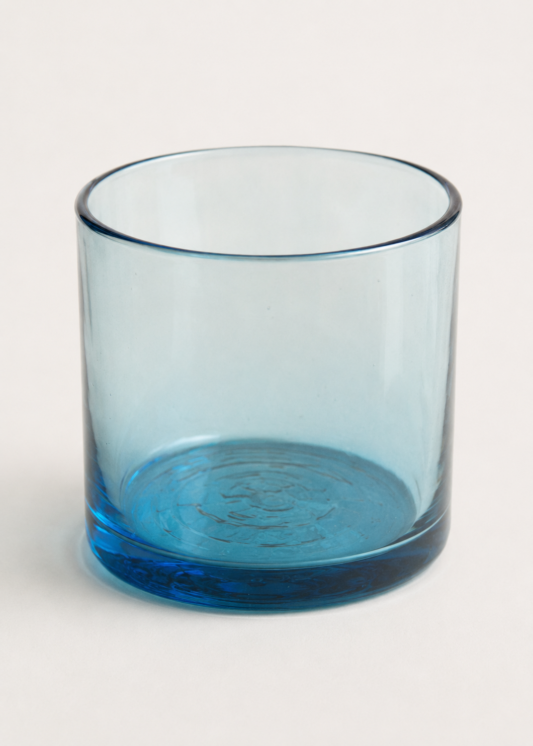 Detalle de vaso azul de vidrio soplado con borde fino y base gruesa.