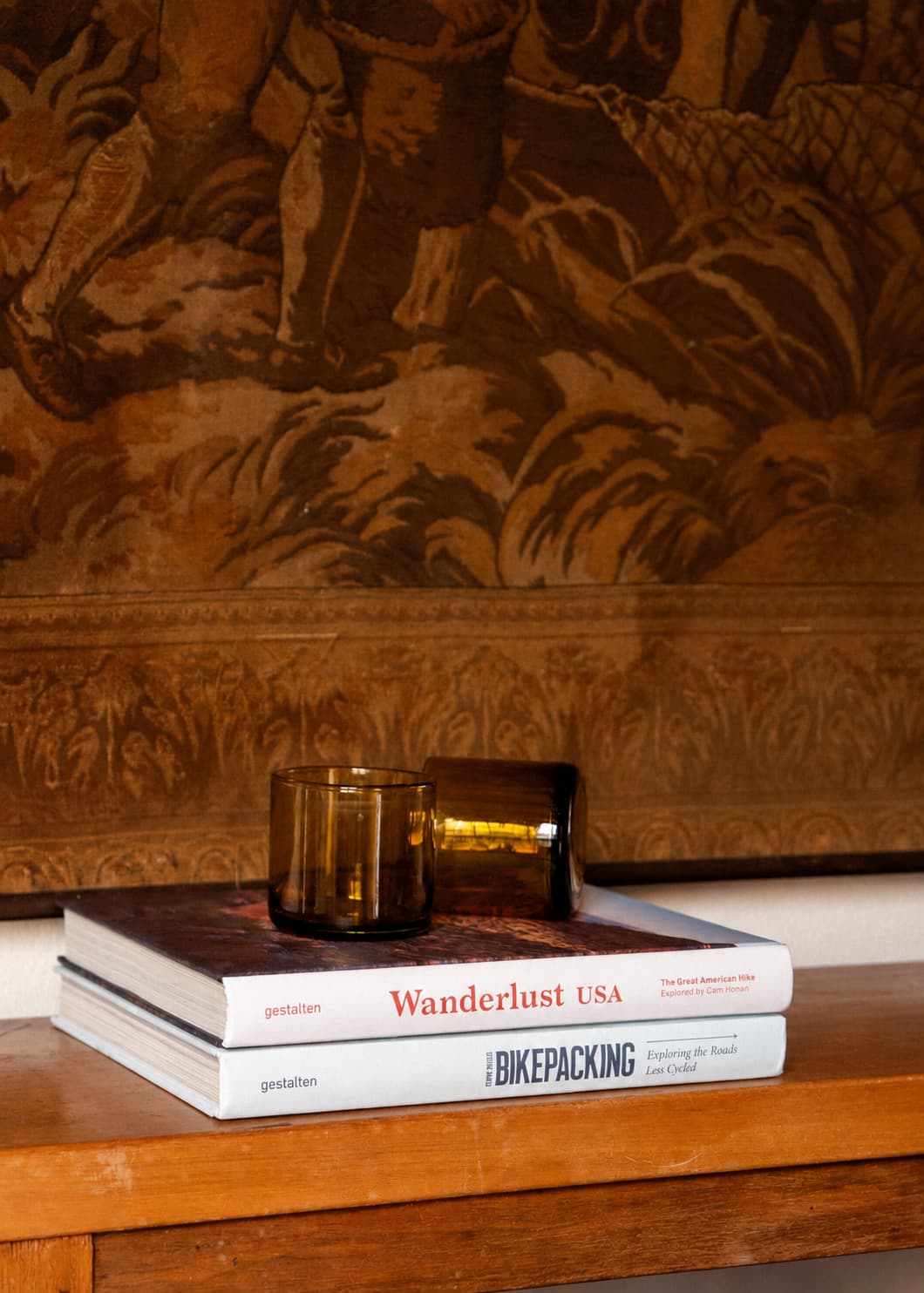 Dos Vasos Cortos Ámbar en vidrio soplado sobre libros, acompañado de una segunda pieza en ambiente interior.