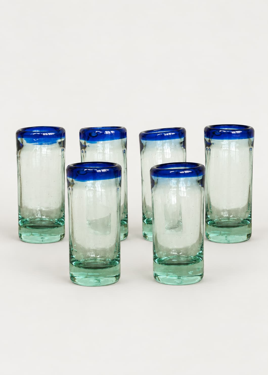 Set de seis vasos de shot con base verde agua y borde azul sobre fondo gris claro.