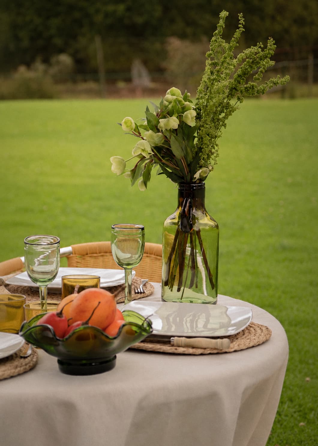 Botella con Asa en vidrio soplado con flores sobre mesa servida en jardín.
