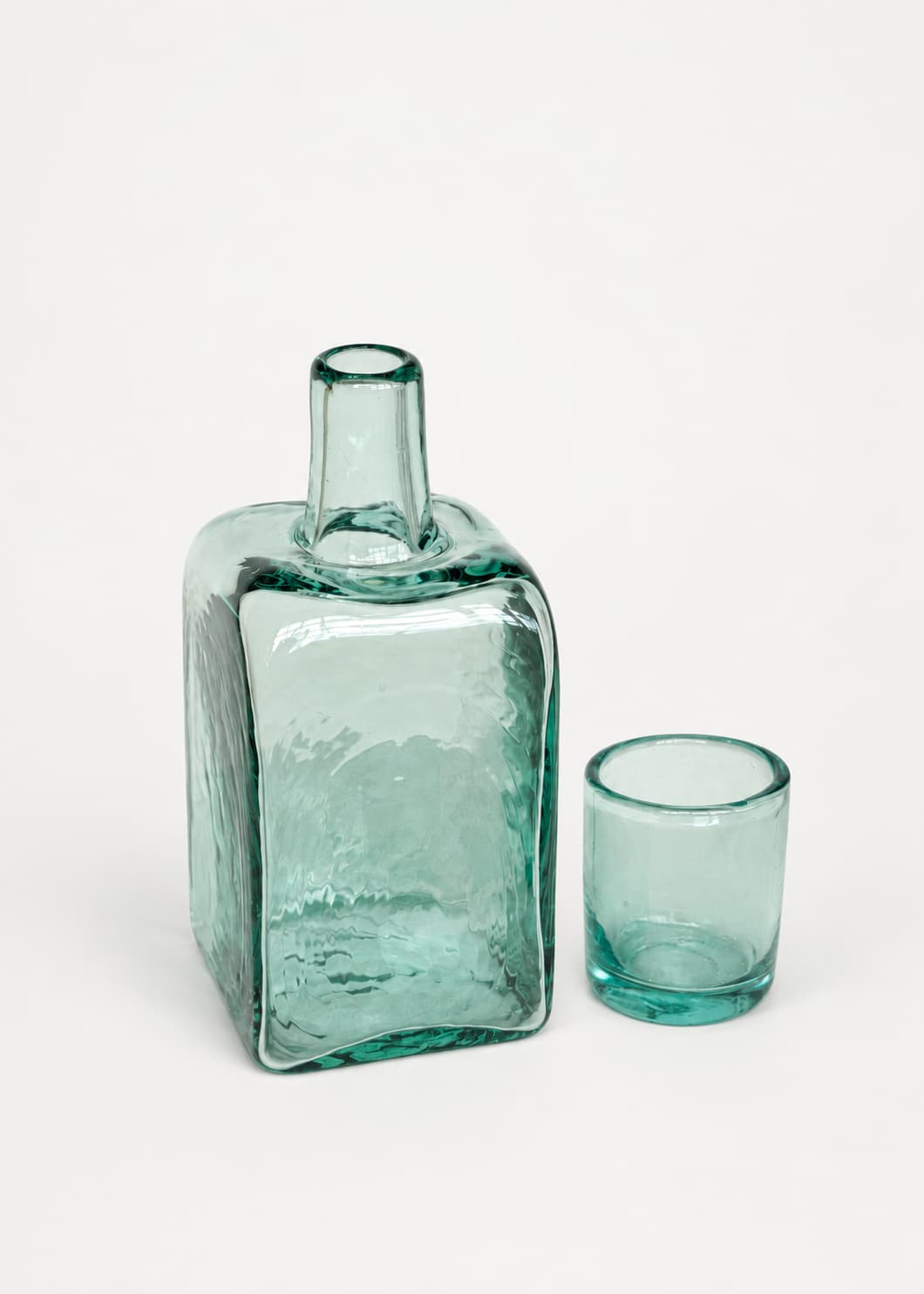 Botella para nochero con vaso en vidrio soplado transparente, con vaso separado junto a la pieza.