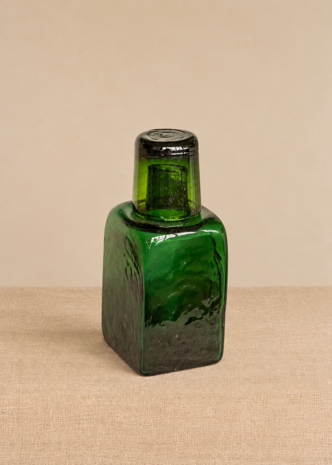 Botella para nochero con vaso en vidrio soplado verde, con el vaso superior funcionando como tapa.
