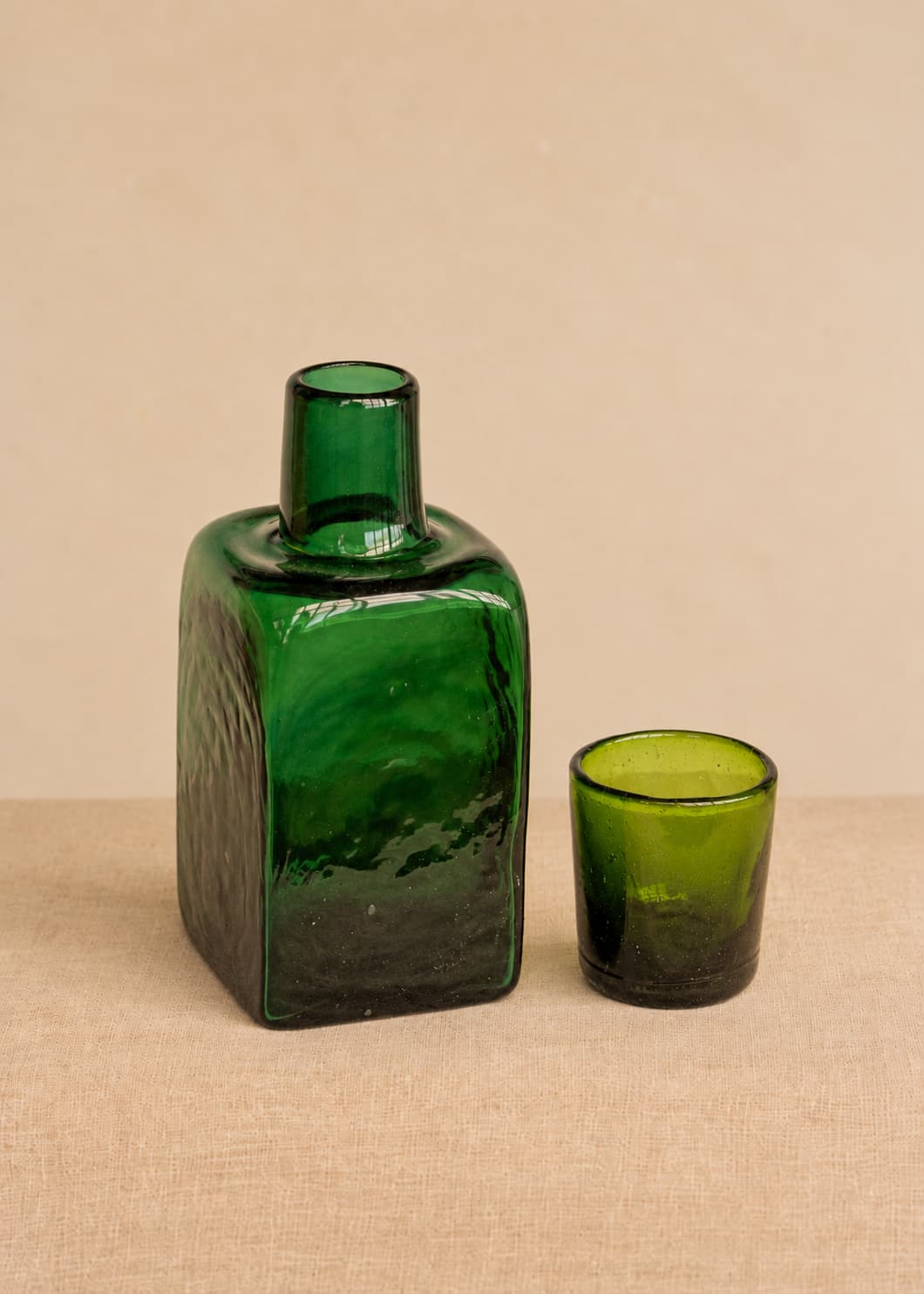 Botella para nochero con vaso en vidrio soplado verde, con vaso separado junto a la pieza.