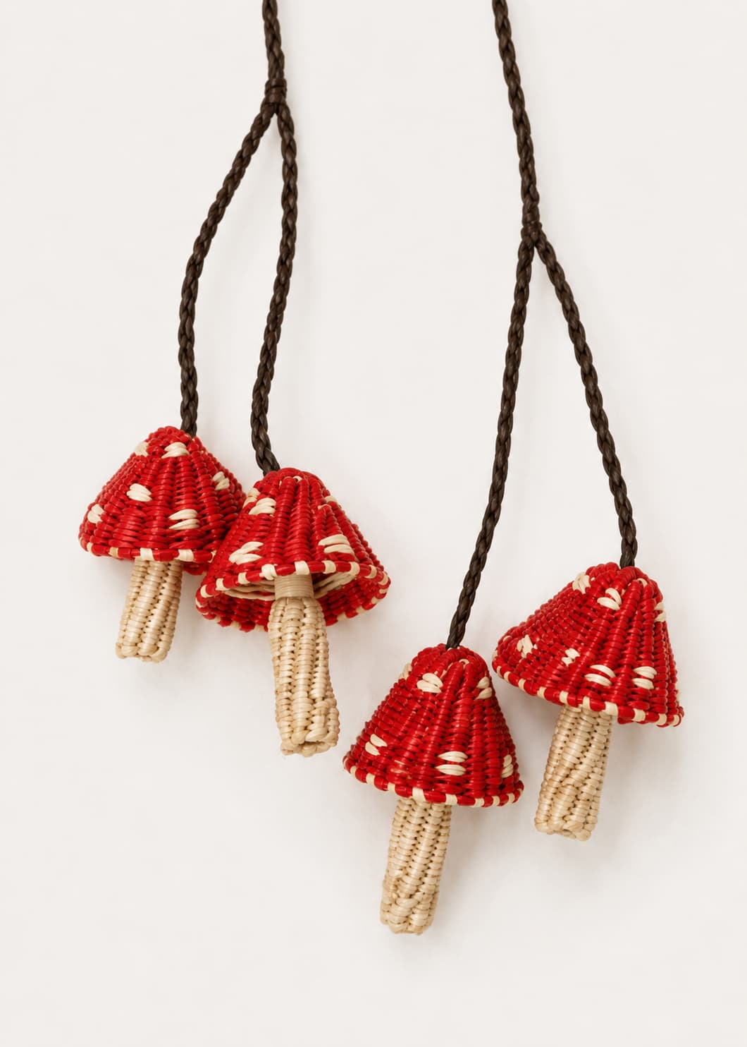 Detalle charm de cuatro hongos rojos tejidos en palma de iraca con cordones trenzados.