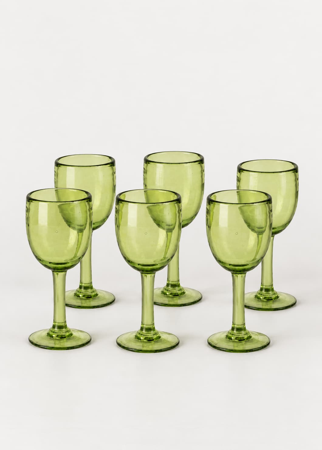 Set de seis copas de vino altas verdes de vidrio soplado, sobre fondo gris claro.