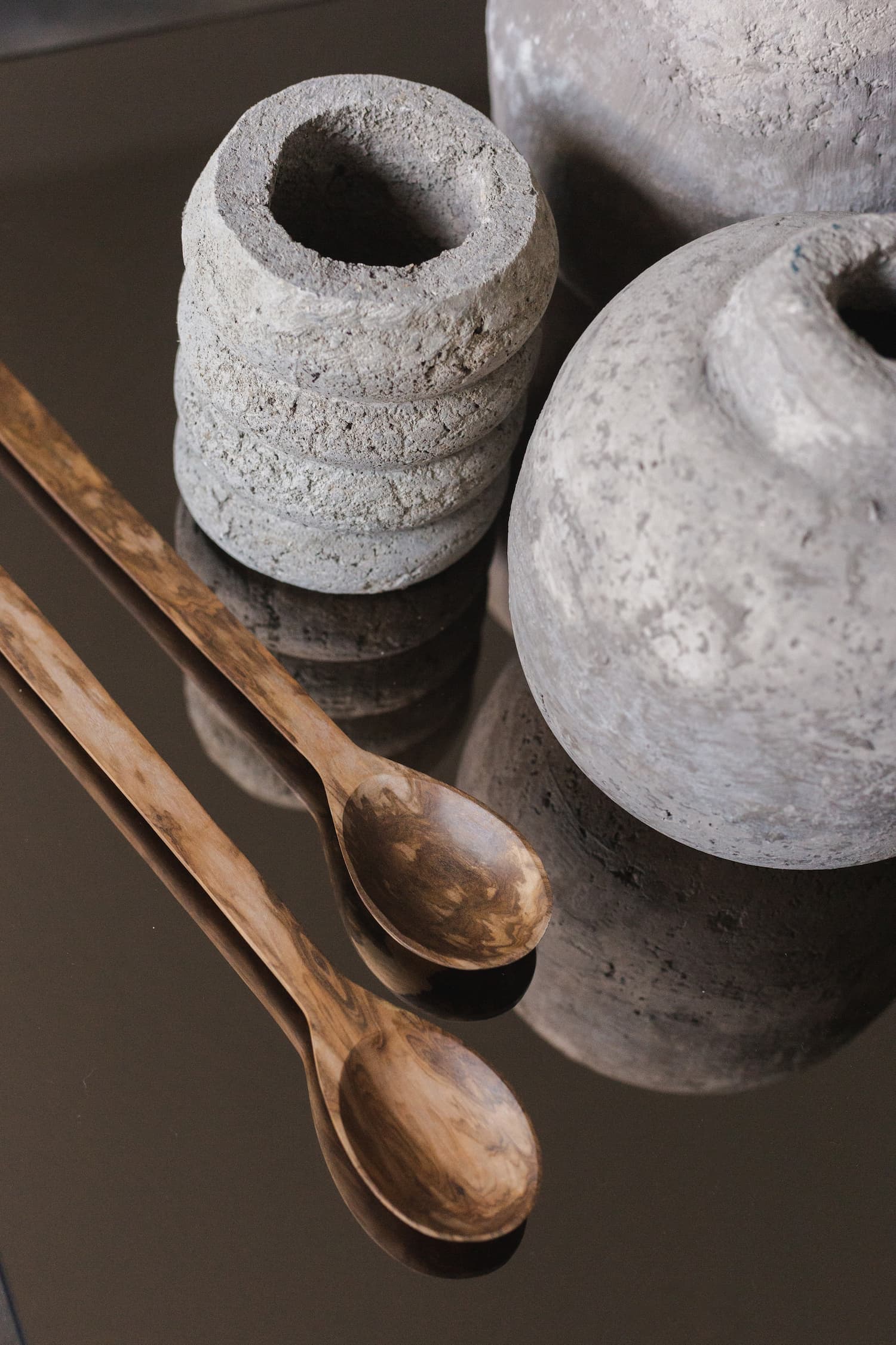 Detalle de cucharas de madera y piezas decorativas sobre una mesa de vidrio en una composición editorial.