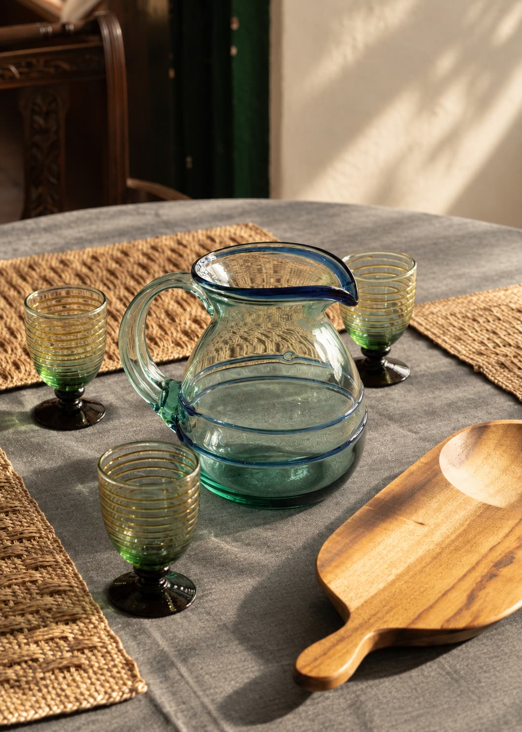 Jarra Dos Hilos Azul de vidrio soplado reciclado en una mesa con individuales tejidos, vasos y bandeja de madera.