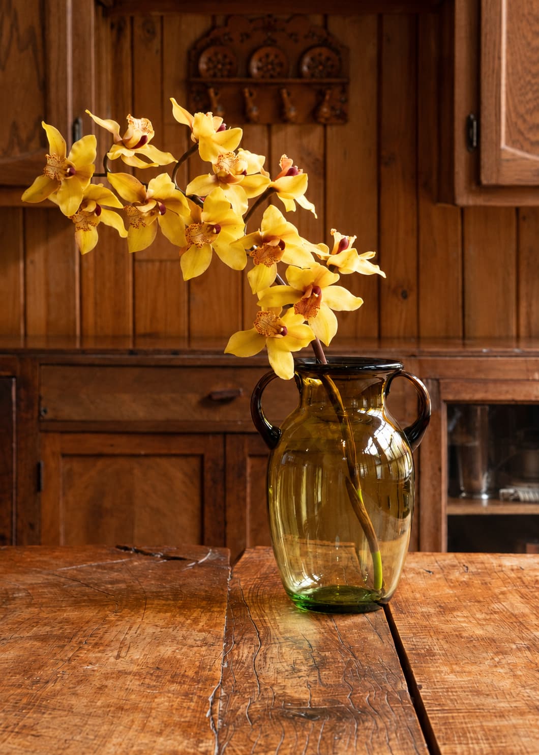 Jarrón Ánfora en vidrio soplado con flores amarillas sobre mesa de madera en ambiente de cocina.