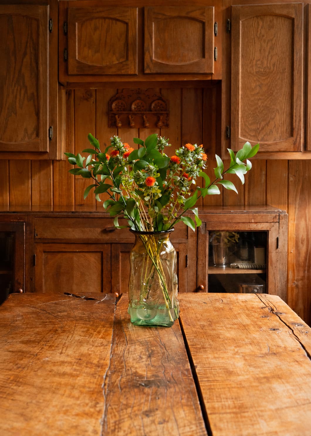 Jarrón Búho en vidrio soplado verde con flores y follaje, sobre una mesa de madera en una cocina.