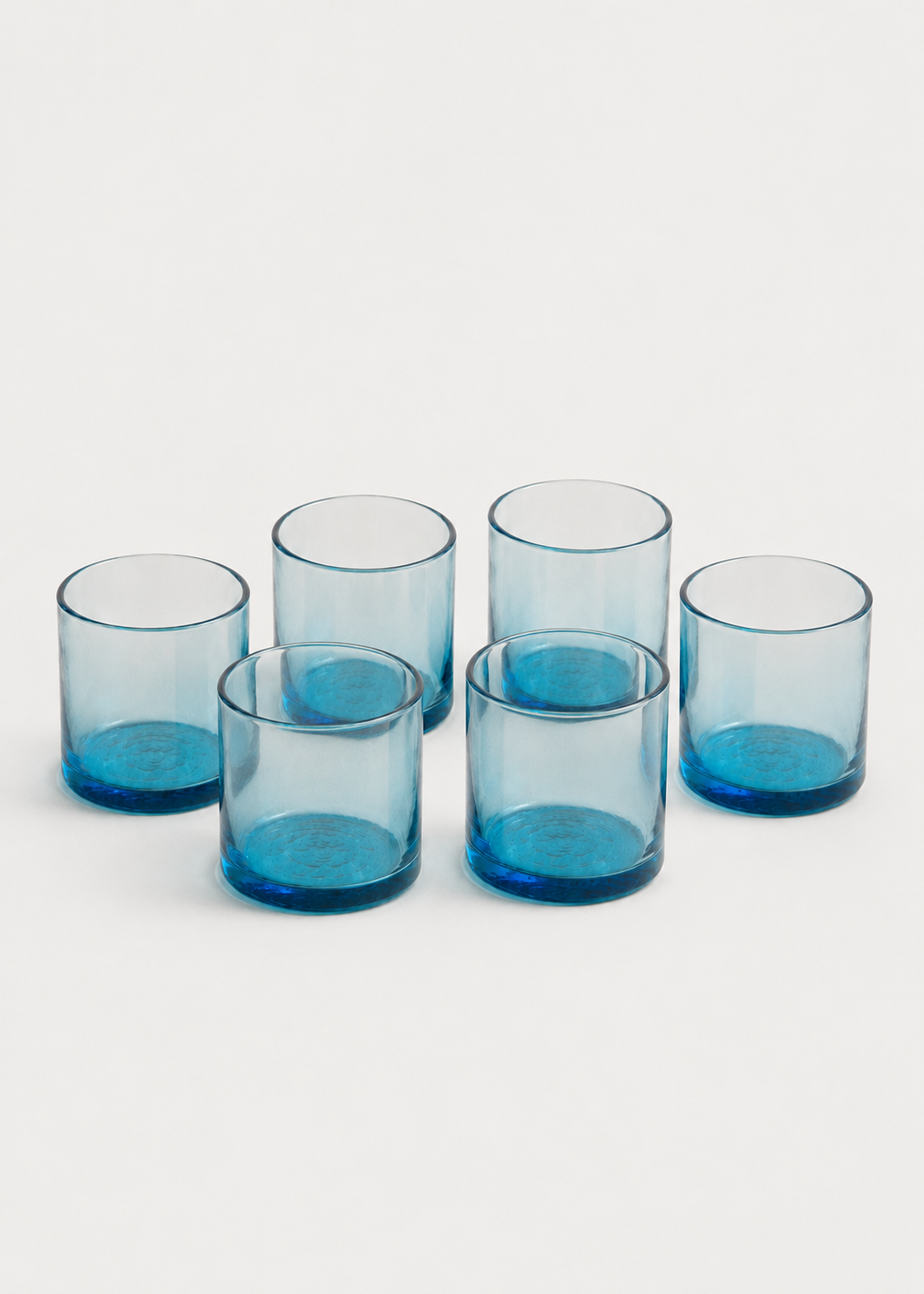 Set de seis vasos azules de vidrio soplado  dispuestos sobre fondo gris claro.