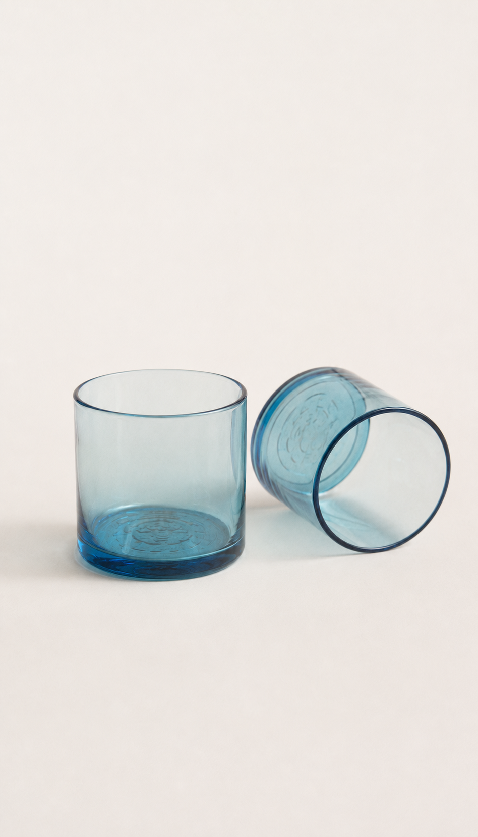 Dos vasos azules de vidrio soplado, uno vertical y otro de lado, sobre fondo gris claro.