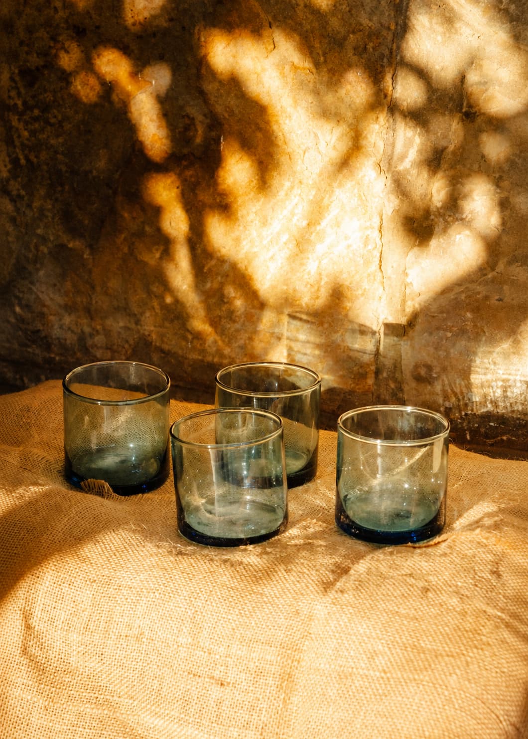 Cuatro vasos azules de vidrio soplado  dispuestos sobre mesa con luz natural.