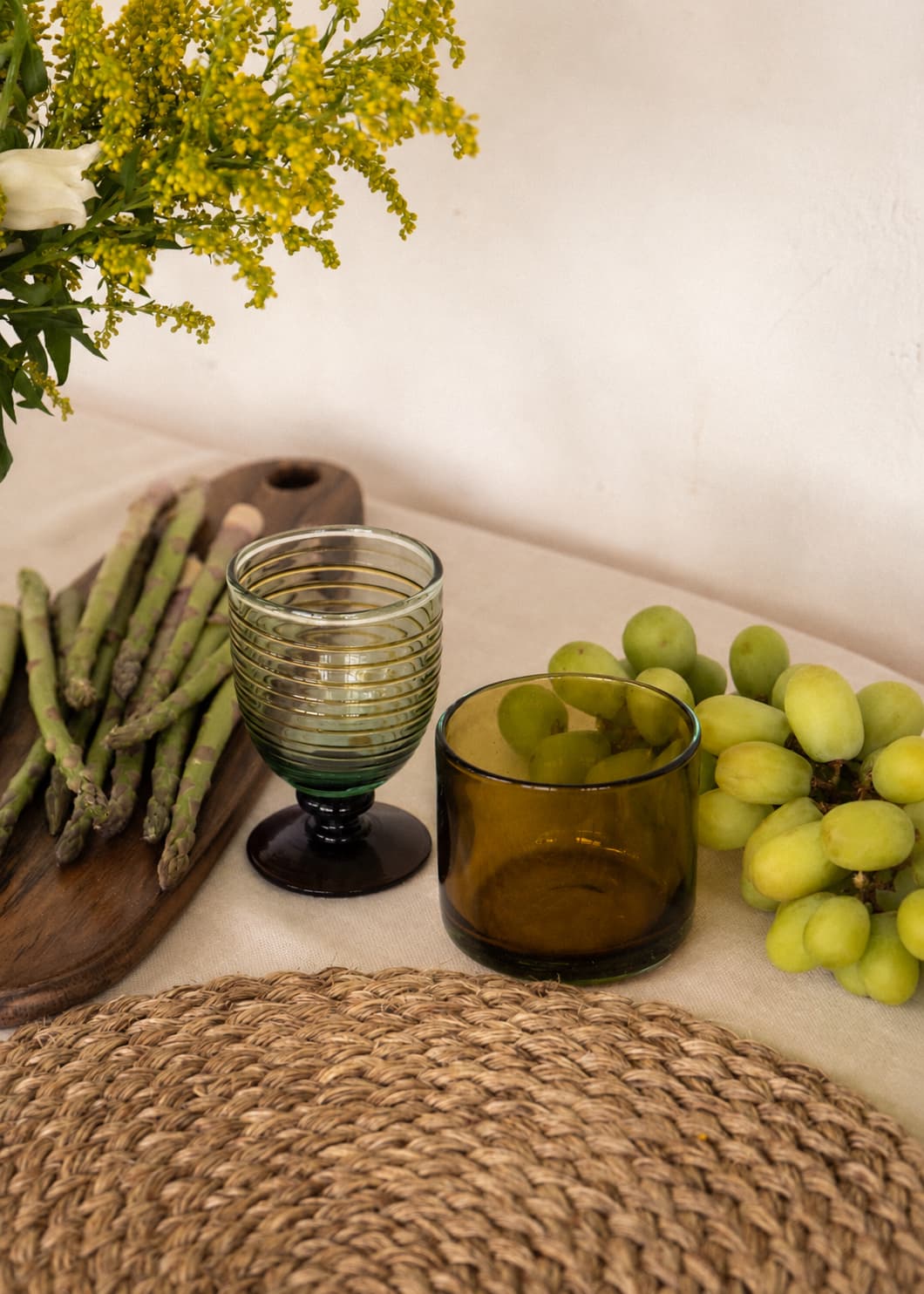 Vaso Bicolor en vidrio soplado sobre mesa, acompañado de copa de vidrio, uvas verdes y espárragos.