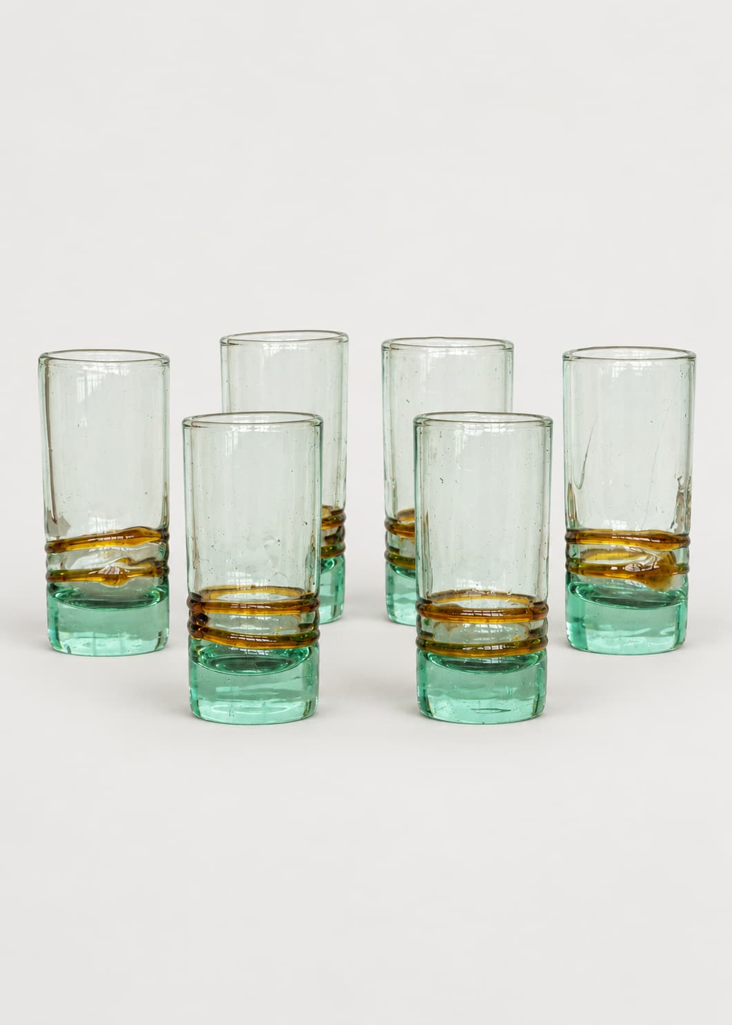 Set de seis vasos de shot con base verde agua y dos hilos ámbar sobre fondo gris claro.